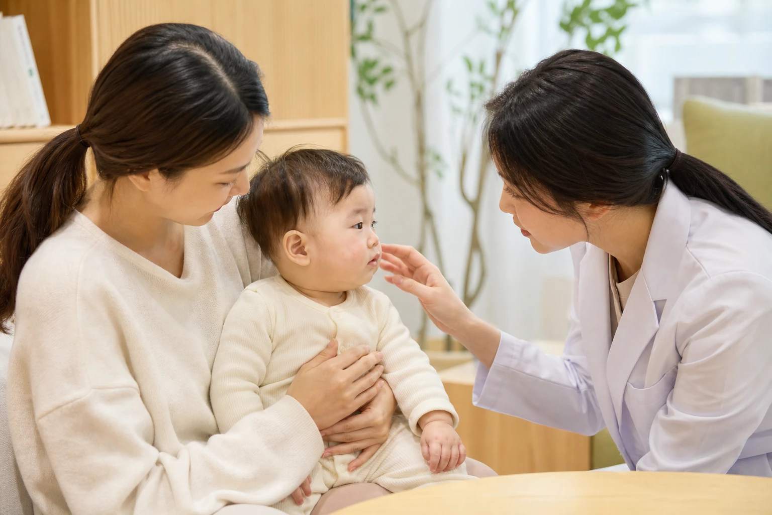 태열이 있는 영아의 볼 피부를 보호자와 여성 한의사가 살피는 진료 장면