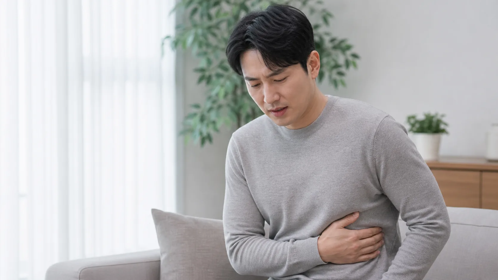 한국인 환자가 실내에서 옆구리 갈비뼈 부위를 짚고 숨쉴 때 통증을 설명하는 장면