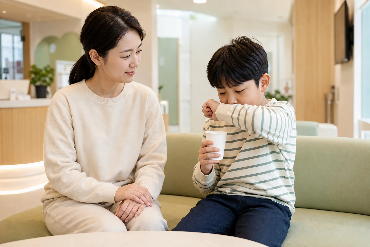 기침 뒤 따뜻한 물을 마시는 아이를 보호자가 살피며 진료를 기다리는 장면