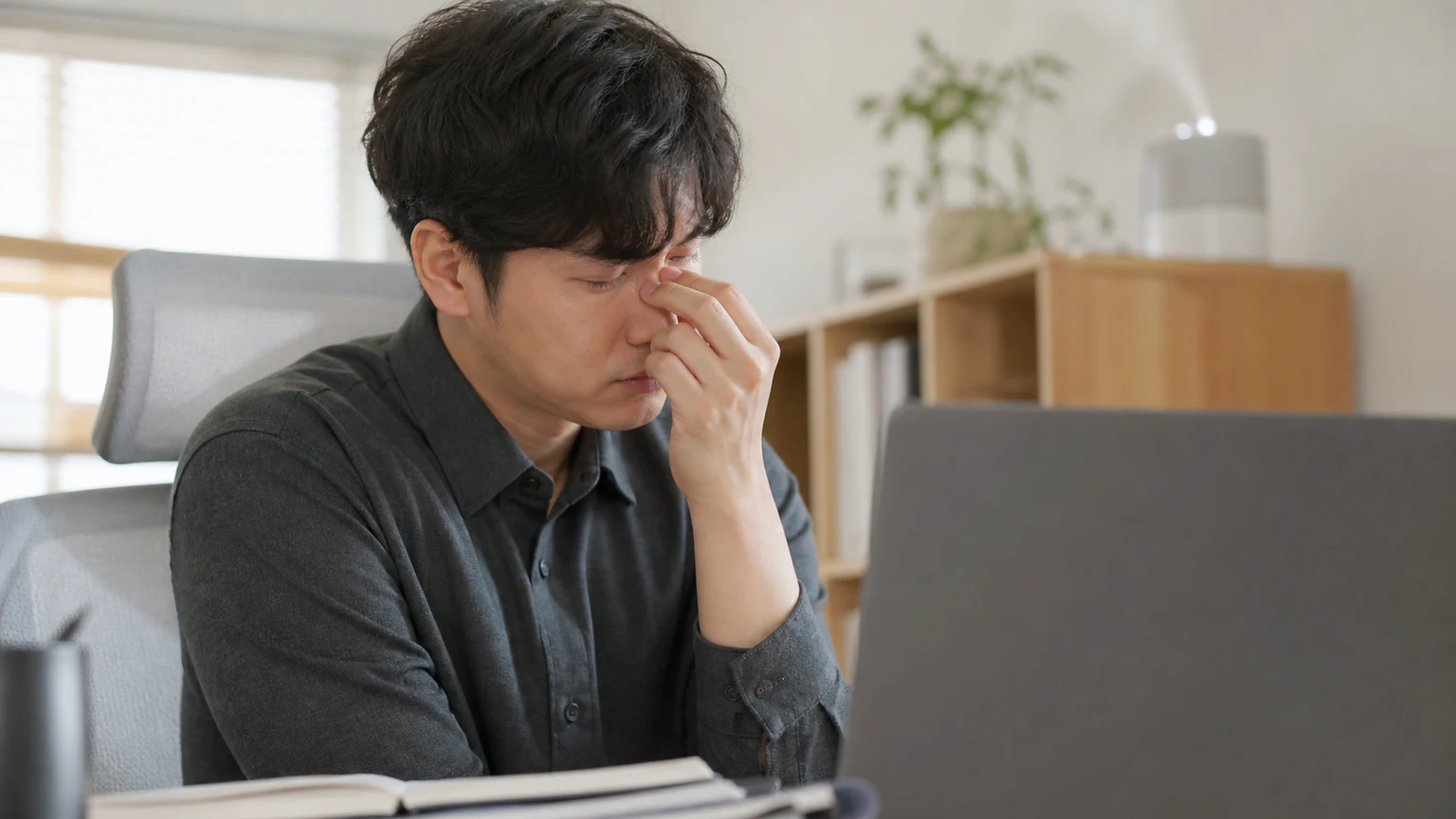노트북 앞에서 눈을 감고 콧등을 짚은 남성