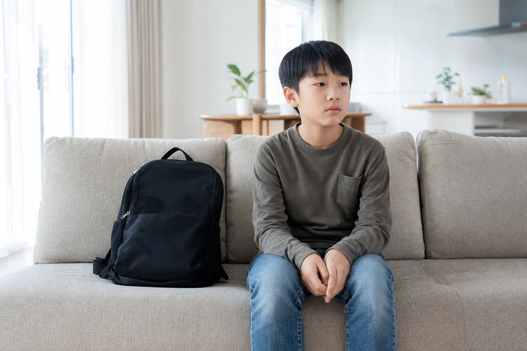 가방을 옆에 두고 두 손을 모아 소파에 앉아 있는 남자아이